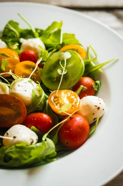 Salada com rúcula, tomate e mussarela sobre fundo de madeira — Fotografia de Stock