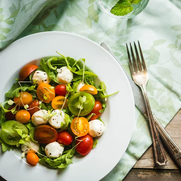 Salat mit Rucola, Tomaten und Mozarella auf Holzgrund — Stockfoto