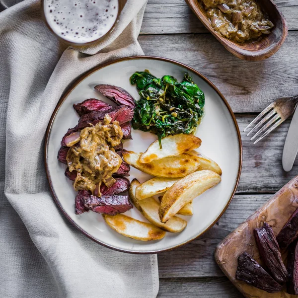 Steak met gebakken botatoes en groene salade op houten achtergrond — Stockfoto