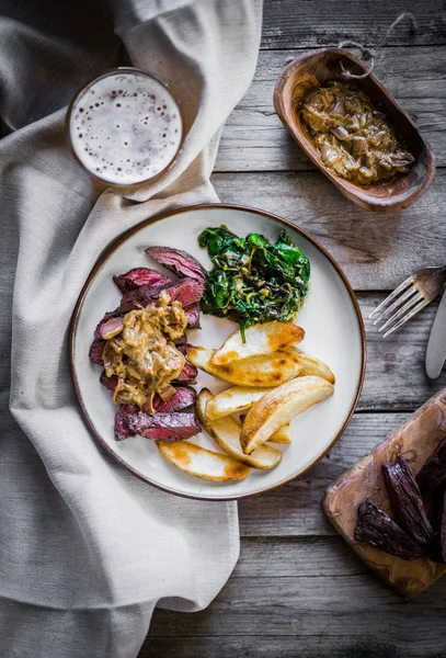 Steak met gebakken botatoes en groene salade op houten achtergrond — Stockfoto