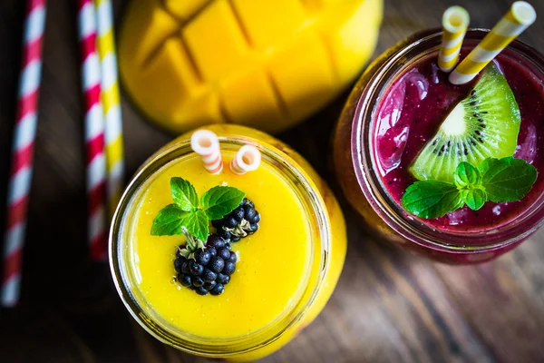 Bunte zweischichtige Smoothies mit Mango und Beeren auf rustikalem — Stockfoto