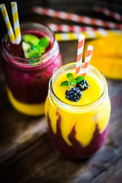 Colorful two layer smoothies with mango and berries on rustic wo — Stock Photo, Image