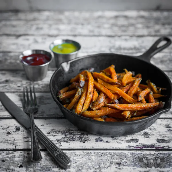 Batat frites i gjutjärn stekpanna på trä bakgrund — Stockfoto