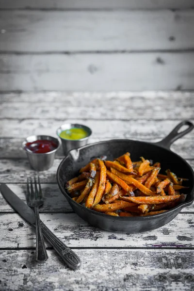 Süßkartoffelfrites in gusseiserner Pfanne auf hölzernem Hintergrund — Stockfoto