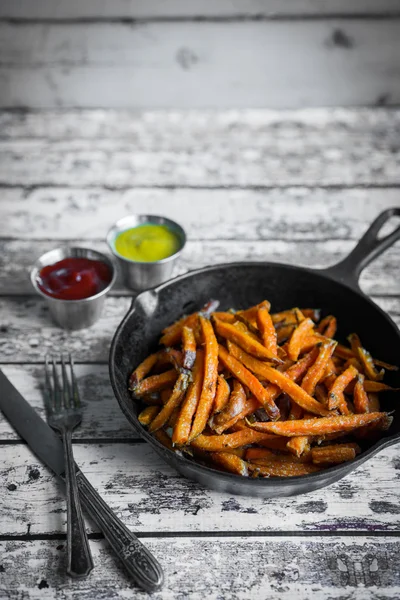 Zoete aardappel frietjes in gietijzer koekepan op houten achtergrond — Stockfoto