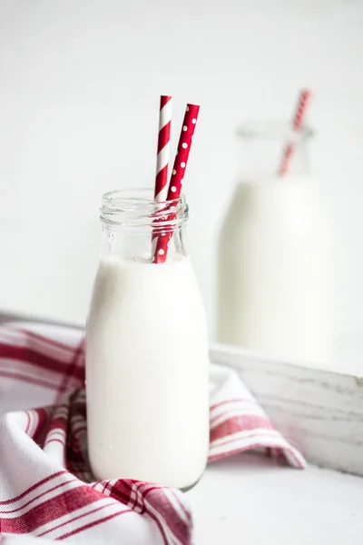 Milk jar with red striped straws on white wooden background — Stock Photo, Image