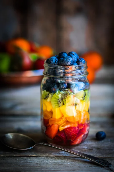 Colorful fruit salad in a jar on rustic wooden background — Stock Photo, Image