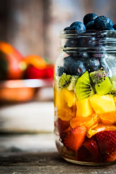 Bir kavanoza rustik ahşap arka plan üzerinde renkli meyve salatası