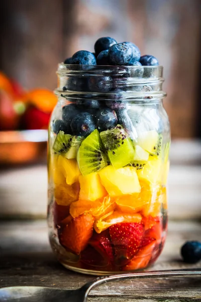 Salada de frutas colorida em um frasco em fundo de madeira rústica — Fotografia de Stock