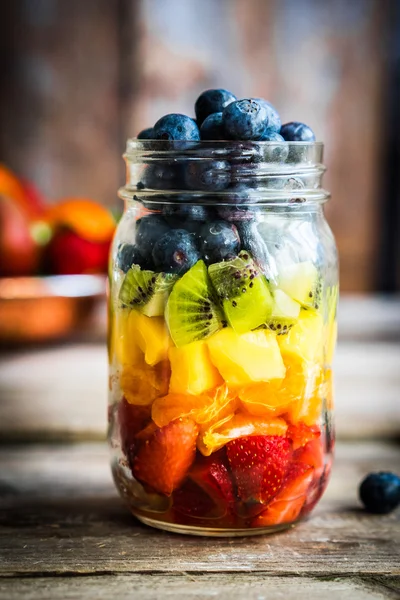 Ensalada de frutas coloridas en un frasco sobre fondo rústico de madera — Foto de Stock