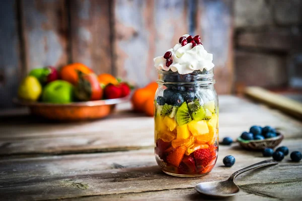 Ensalada de frutas coloridas en un frasco sobre fondo rústico de madera —  Fotos de Stock