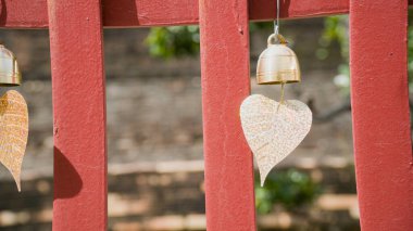 Yeşil yapraklarla çevrili, kırmızı ahşap bir yapıda asılı duran kalp şeklinde bir dekorasyon sıcak ve davetkar bir atmosfer yaratıyor..