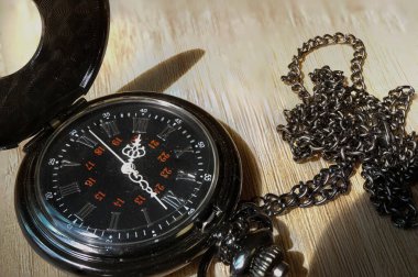 Karmaşık tasarım ve zincirli antik cep saati, ahşap bir yüzeye yerleştirilmiş, zarafet ve klasik tarzı sergiliyor..