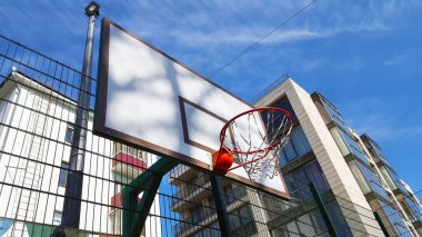 Arka bahçedeki çocuk parkı. Arka planda basketbol potası ve mavi gökyüzü.