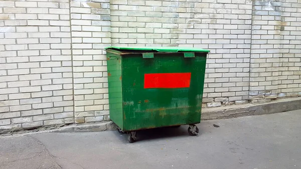 green old trash can near white brick wall