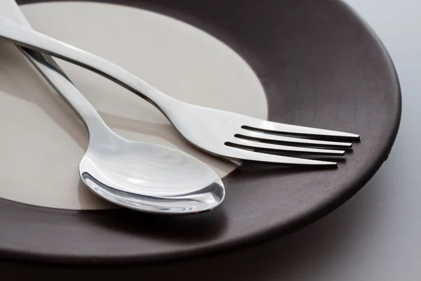Тарілки зі срібною вилкою і ложкою ізольовані на сірому фоні — стокове фото