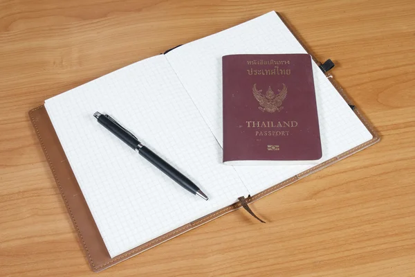 Notebook aberto com passaporte e caneta sobre fundo de madeira — Fotografia de Stock