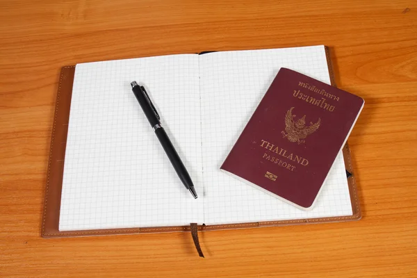 Notebook aberto com passaporte e caneta sobre fundo de madeira — Fotografia de Stock