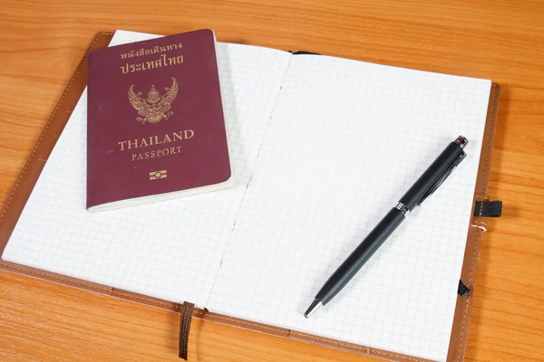 Notebook aberto com passaporte e caneta sobre fundo de madeira — Fotografia de Stock