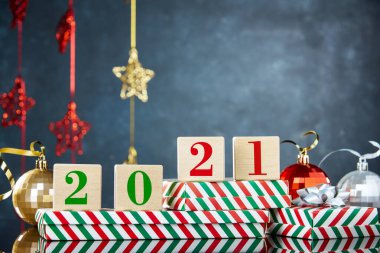 Kutunun üzerinde 2021 rakamları olan küplerin arka planında Noel süslemeleri olan bir Noel hediyesi. Yeni yıl arkaplanı, metin için boş alan.
