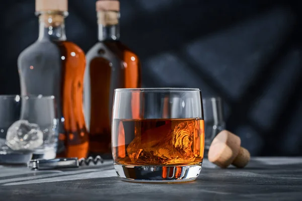 Round glass of whiskey with ice on a concrete table, on a blue background. Round glass of brandy with ice on a concrete table, on a blue background.