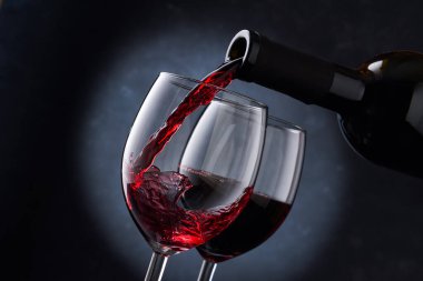 Kırmızı şarap, bulanık mavi arka plandaki bir şişeden bardağa dökülüyor. Kırmızı şarap, bardaktaki girdabın içinde, yakın plan..