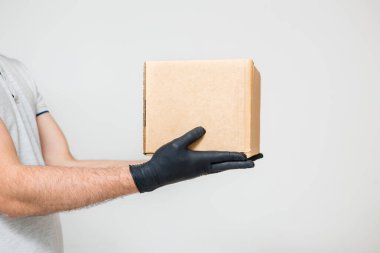 Tıbbi lastik eldivenli ve koruyucu maskeli bir kurye karton kutu tutuyor. Teslimat servisi. Karantina.