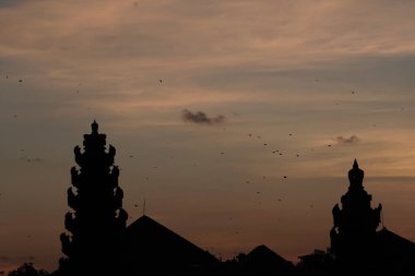 Bali 'de tapınak ve geleneksel Bali uçurtmaları manzaralı bir yerde güneş batarken öğleden sonra silueti. Gökyüzü turuncu ve mavidir.