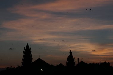 Bali 'de tapınak ve geleneksel Bali uçurtmaları manzaralı bir yerde güneş batarken öğleden sonra silueti. Gökyüzü turuncu ve mavidir.