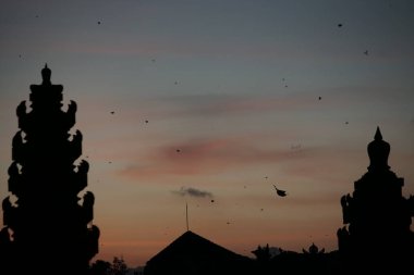 Bali 'de tapınak ve geleneksel Bali uçurtmaları manzaralı bir yerde güneş batarken öğleden sonra silueti. Gökyüzü turuncu ve mavidir.