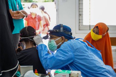 BALI / INDONESIA-MAY 28 2021: Bir ENT doktoru bir pediyatrik hastanın kulaklarını, burnunu ve boğazını muayene ediyor. COVID-19 salgını sırasında, ENT incelemeleri çok risklidir çünkü virüsün bulunduğu organlardaki hastalarla doğrudan temasta bulunurlar. 