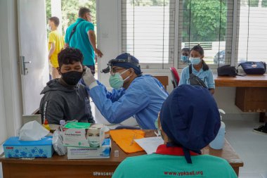 BALI / INDONESIA-MAY 28 2021: Bir ENT doktoru bir pediyatrik hastanın kulaklarını, burnunu ve boğazını muayene ediyor. COVID-19 salgını sırasında, ENT incelemeleri çok risklidir çünkü virüsün bulunduğu organlardaki hastalarla doğrudan temasta bulunurlar. 