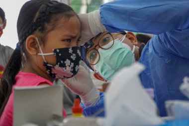 BALI / INDONESIA-MAY 28 2021: Bir ENT doktoru bir pediyatrik hastanın kulaklarını, burnunu ve boğazını muayene ediyor. COVID-19 salgını sırasında, ENT incelemeleri çok risklidir çünkü virüsün bulunduğu organlardaki hastalarla doğrudan temasta bulunurlar. 
