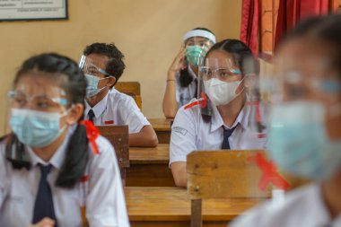 BALI, INDONESIA-MAY 18 2021: Endonezya 'daki öğrenciler COVID-19 salgını sırasında sağlık protokollerini uygulamak için yüz maskeleri ve sağlık maskeleri kullanarak öğrenme sürecini takip ediyorlar