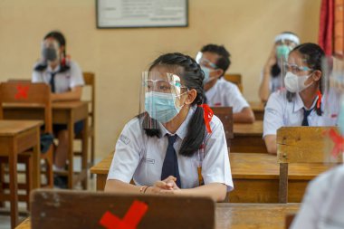 BALI, INDONESIA-MAY 18 2021: Endonezya 'daki öğrenciler COVID-19 salgını sırasında sağlık protokollerini uygulamak için yüz maskeleri ve sağlık maskeleri kullanarak öğrenme sürecini takip ediyorlar