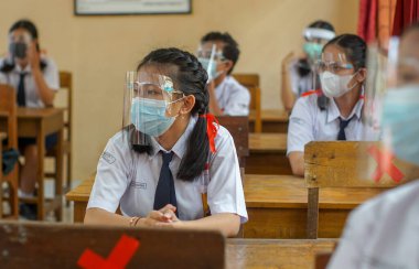 BALI, INDONESIA-MAY 18 2021: Endonezya 'daki öğrenciler COVID-19 salgını sırasında sağlık protokollerini uygulamak için yüz maskeleri ve sağlık maskeleri kullanarak öğrenme sürecini takip ediyorlar