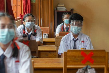 BALI, INDONESIA-MAY 18 2021: Endonezya 'daki öğrenciler COVID-19 salgını sırasında sağlık protokollerini uygulamak için yüz maskeleri ve sağlık maskeleri kullanarak öğrenme sürecini takip ediyorlar