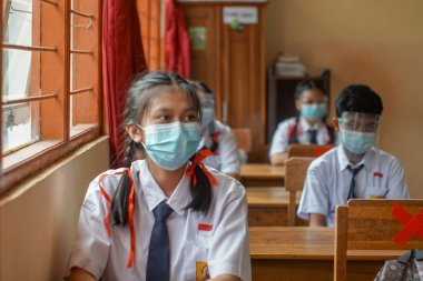 BALI, INDONESIA-MAY 18 2021: Endonezya 'daki öğrenciler COVID-19 salgını sırasında sağlık protokollerini uygulamak için yüz maskeleri ve sağlık maskeleri kullanarak öğrenme sürecini takip ediyorlar