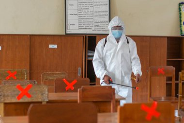 BALI, İNDONEZYA-MAYIS 18-2021: sağlık görevlileri sınıf alanını ilaçlıyor. Endonezya, salgın sırasında bir yıldan uzun süre kapalı kaldıktan sonra okullarındaki faaliyetleri yeniden başlatacak