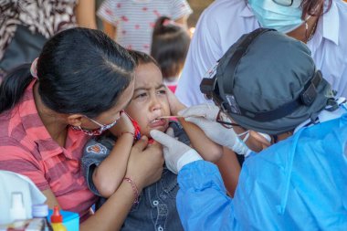 BALI / INDONESIA-MAY 28 2021: Bir ENT doktoru bir pediyatrik hastanın kulaklarını, burnunu ve boğazını muayene ediyor. COVID-19 salgını sırasında, ENT incelemeleri çok risklidir çünkü virüsün bulunduğu organlardaki hastalarla doğrudan temasta bulunurlar. 