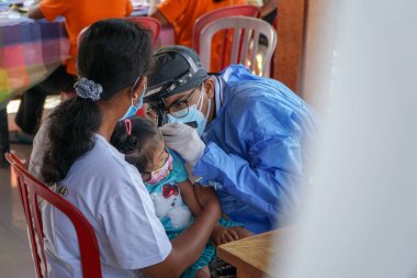 BALI / INDONESIA-MAY 28 2021: Bir ENT doktoru bir pediyatrik hastanın kulaklarını, burnunu ve boğazını muayene ediyor. COVID-19 salgını sırasında, ENT incelemeleri çok risklidir çünkü virüsün bulunduğu organlardaki hastalarla doğrudan temasta bulunurlar. 