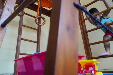 Yeni yürümeye başlayan bir çocuk etkin bir şekilde kolunda oynuyordu ve tırmanıyordu. Oyuncaklarıyla mutlu ve neşeli görünüyor.