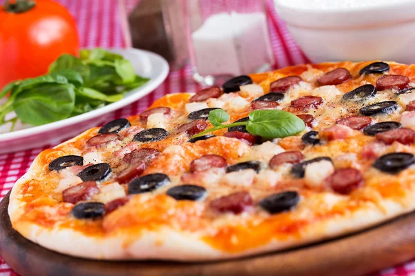 Homemade pizza with hunter sausages, bacon, olives and basil — Stock Photo, Image