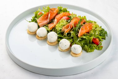 Beyaz tabakta peynirli somon salatası.