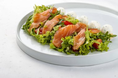 Beyaz tabakta peynirli somon salatası.