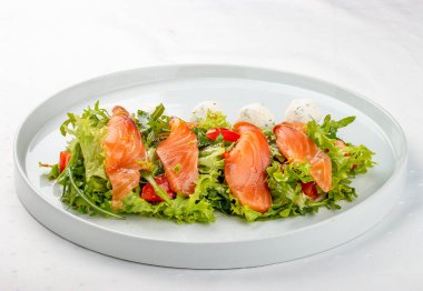 Beyaz tabakta peynirli somon salatası.