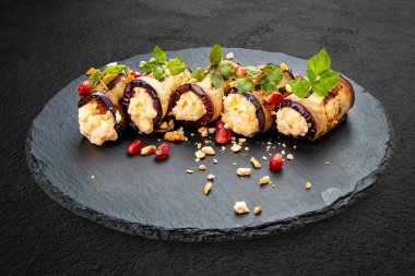 Peynir ve fındıkla doldurulmuş patlıcan ruloları, taş bir tahtanın üzerinde.