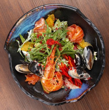 Deniz ürünleri salatası: karides, midye, somon, roka ve portakal. Dekoratif bir tabakta