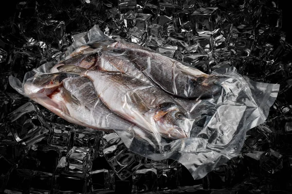 Vacuum-packed fish, on dark ice background, dorada. Semifinished.