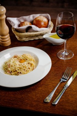 Tahta arka planda beyaz tabakta peynirli ve yumurtalı spagetti.